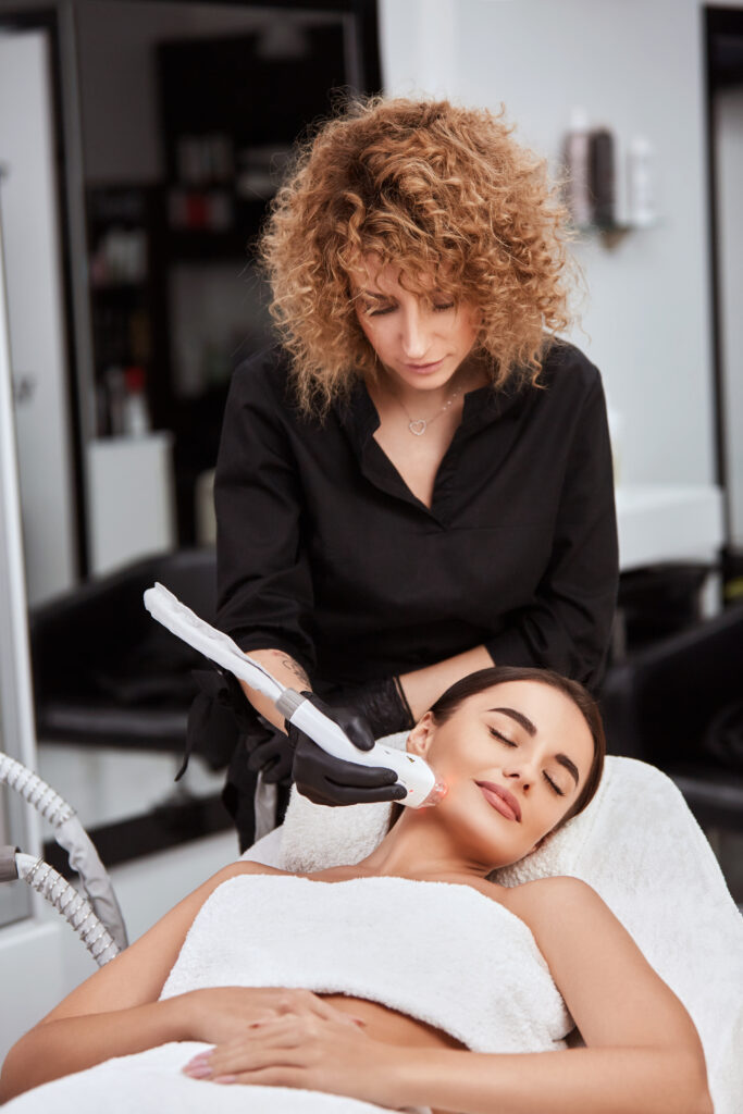 beautician doing laser theraphy on pretty woman face in spa salon