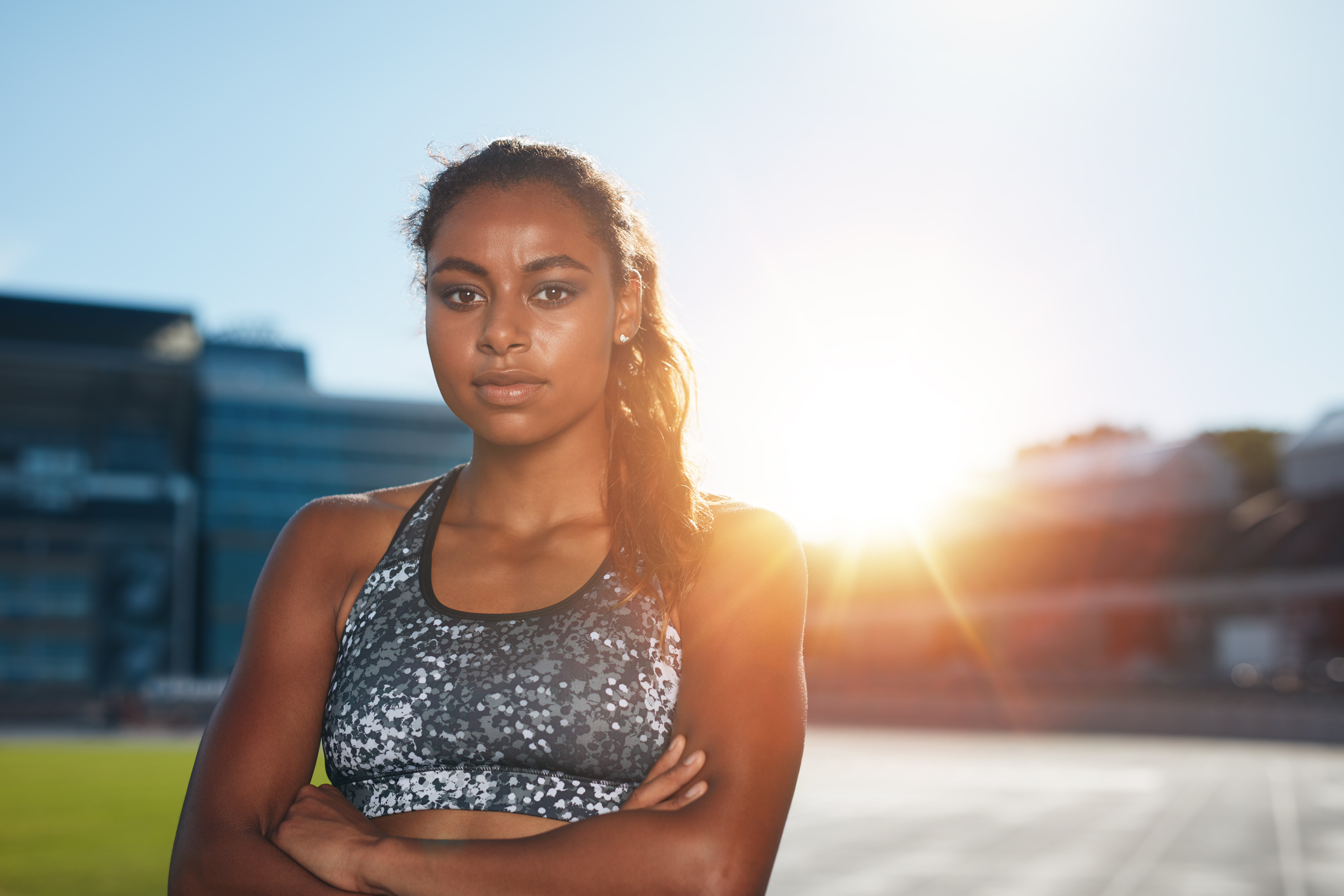 Confident female athlete standing outdoors in the sun with arms crossed