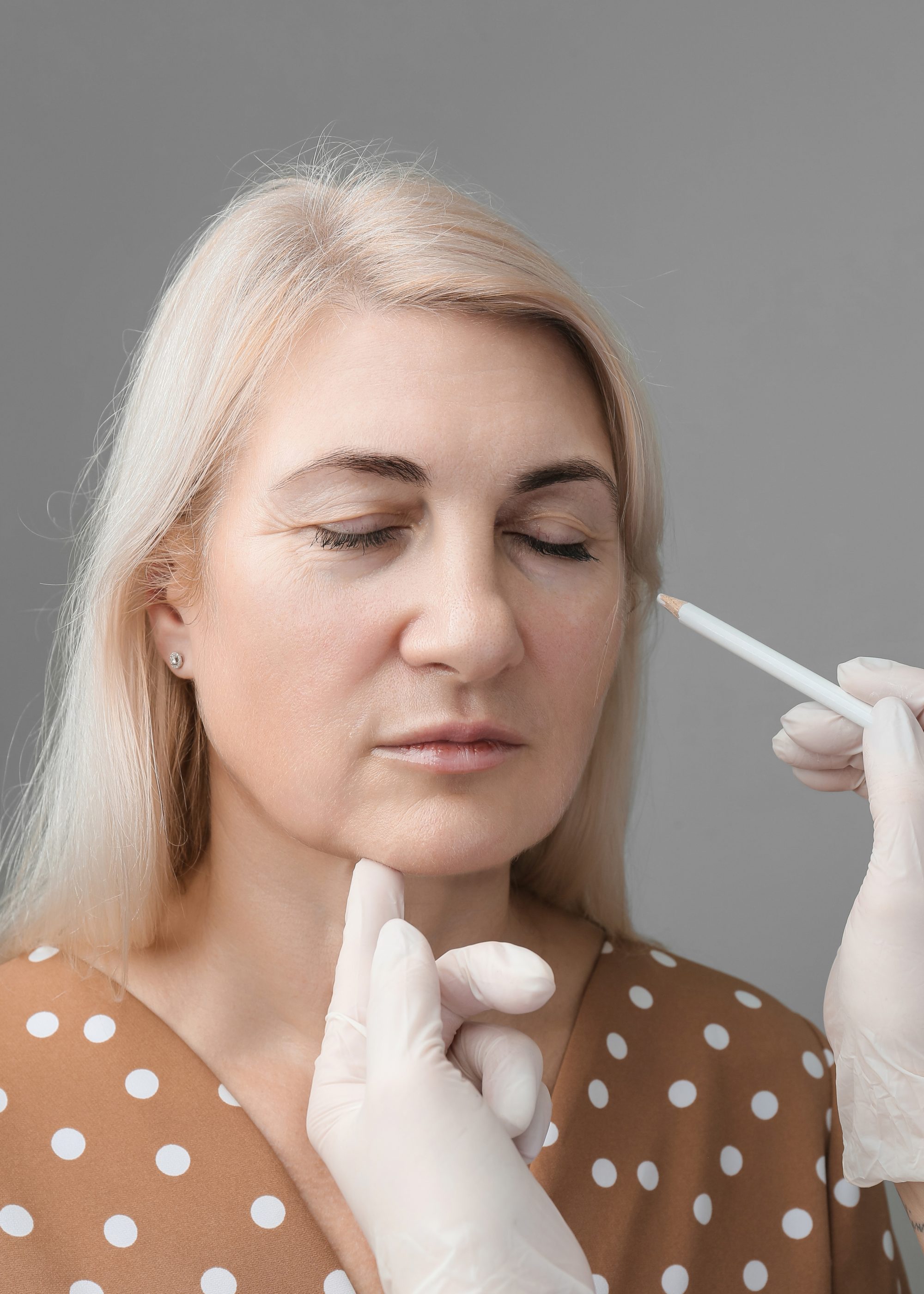 The beautician makes markings on the woman’s face with a white pencil. The beautician makes markings on the woman's face with a white pencil.